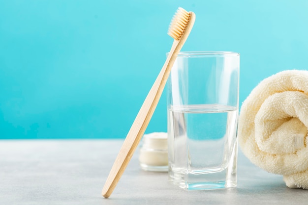 A bamboo toothbrush, a glass of water, a white cotton towel and toothbrush powder in a jar