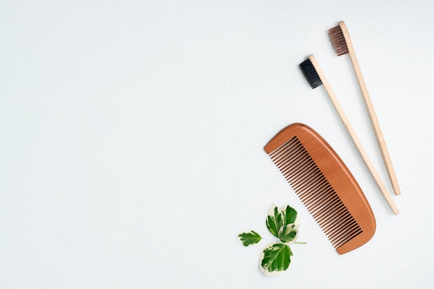 Bamboo toothbrush and wooden comb on a light wall. Zero waste concept, copy space.
