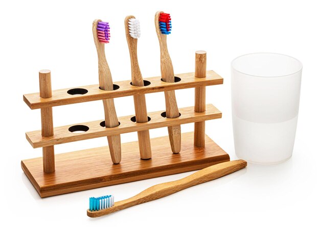 Photo bamboo toothbrushes in a holder with a glass of water isolated on white