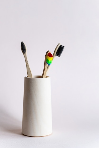 Bamboo toothbrushes in a wooden glass on a light background