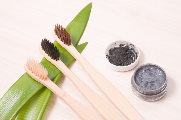 Spazzolini da denti di bambù su una tavola di legno, concetto di stile di vita amichevole di eco del dentifricio in pasta del carbone di legna fatto in casa