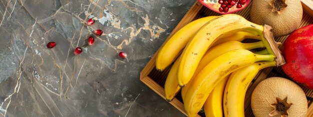 A bamboo tray with bunches of bananas a ripe melon and a pomegranate Grey marble background cop