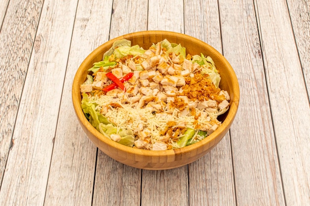 Bamboo wooden bowl with Caesar salad with battered chicken crispy onion iceberg lettuce grated cheese