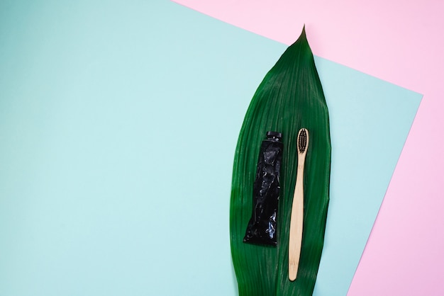 Bamboo wooden brush and toothpaste in a metal tube on a natural palm green leaf. The concept of caring for nature, rejection of plastic