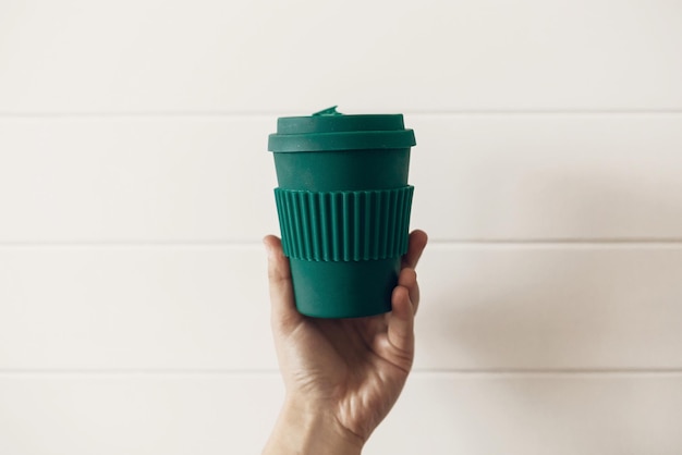 일회용 플라스틱 금지 흰색 나무 배경에 세련된 재사용 가능한 에코 커피 컵을 들고 있는 손 천연 대나무 섬유 제로 폐기물 개념의 녹색 컵 선택 커피를 가져가세요