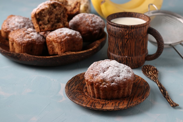 Banaanmuffins met havermoutvlokken bestrooid met poedersuiker op een kokosnotenplaat en kop melk, horizontale oriëntatie