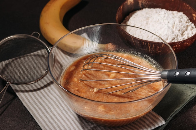 Banana bread mix in transparent bowl on brown background