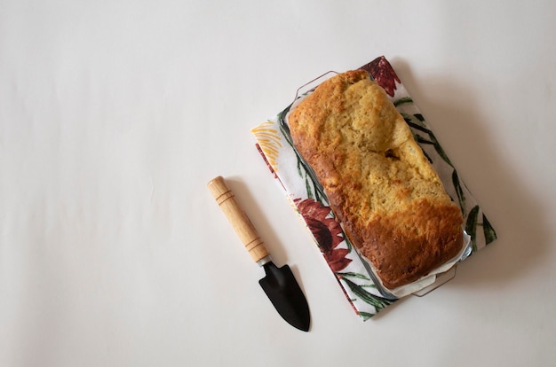Banana bread next to a small shovel on a white background flat lay