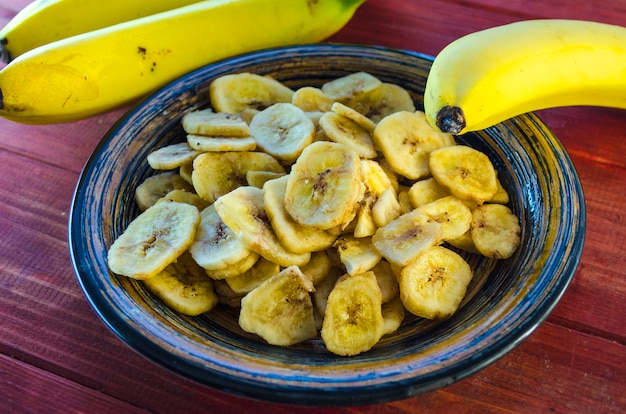 Banana chips in a bowl and fresh bananas