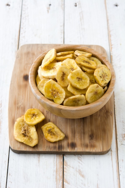 Photo banana chips in bowl on white wooden table