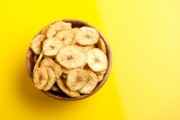 Banana chips in wooden bowl on yellow background