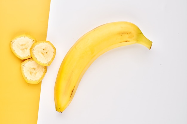 Banana creative background. Yellow and white backdrop with whole, peeled, sliced bananas