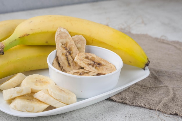 Banana and dried banana chips scattered on grey background