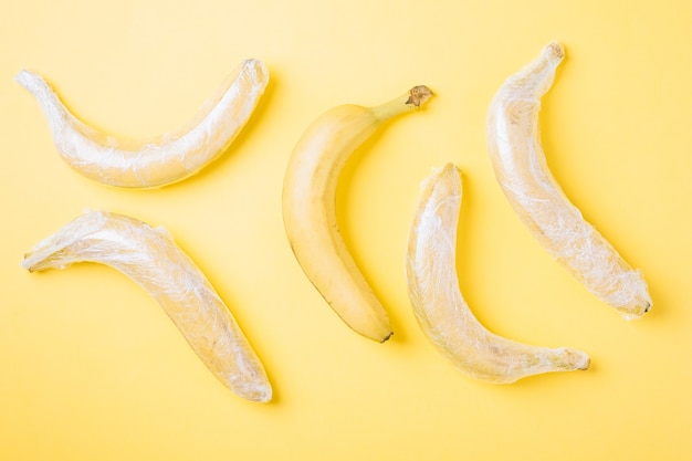 Banana fruits wrapped in stretch plastic on yellow surface