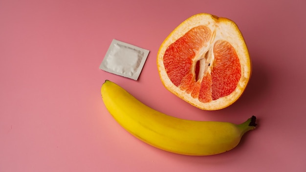 Banana e pompelmo con preservativo su sfondo rosa. concetto di sesso sicuro