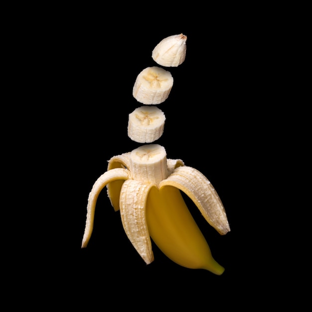 Banana isolated on black surface. Surreal design. Pieces of fruit floating in the air.