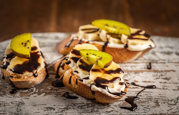 Banana and kiwi dessert with chocolate syrup on the wooden board, fruit sandwiches, fast lunch . High quality photo