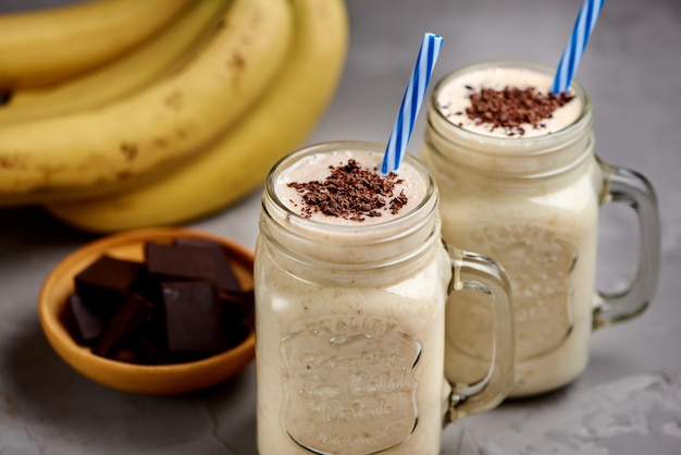 Banana milkshake in a glass with chocolate on grey concrete surface, closeup