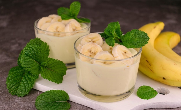 Banana mousse in low glasses with mint on a white board Closeup