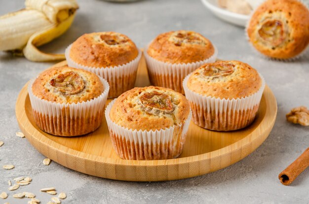 Banana muffins with oatmeal, walnuts and cinnamon on a wooden tray on grey background