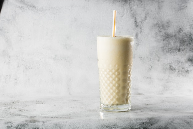 Banana oats smoothie or vanilla milkshake in glass on bright marble background. Overhead view, copy space. Advertising for milkshake cafe menu. Horizontal photo.