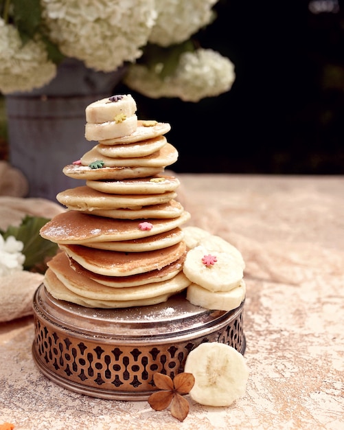 Pancake alla banana con pezzi di frutta e fiori primaverili. vassoio e vaso d'epoca