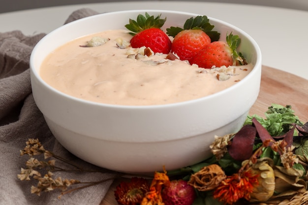 Banana, papaya and coconut smoothie accompanied by Strawberries and Brazil nuts, in a white bowl and decorated with dried flowers.