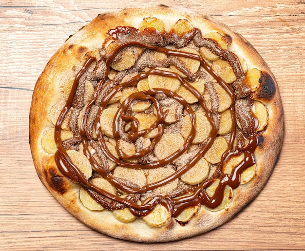 Pizza alla banana con salsa al cioccolato e cannella in polvere, servita su un tavolo di legno