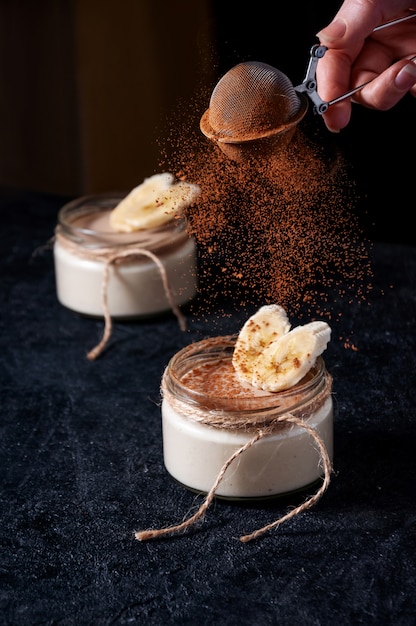 Banana pudding with cocoa powder on dark background