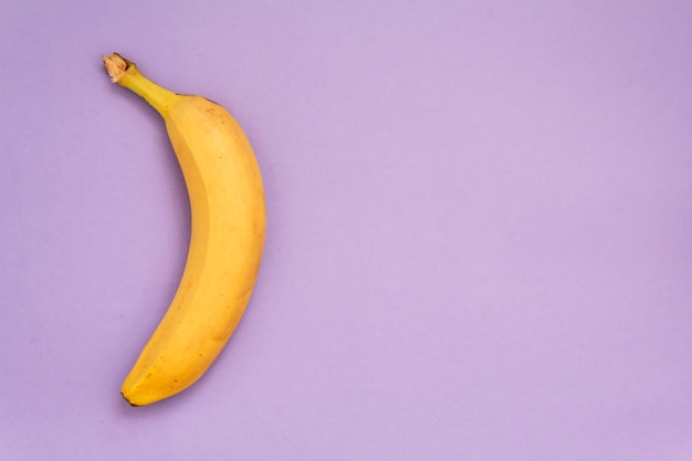 Banana on purple background top view with copy space