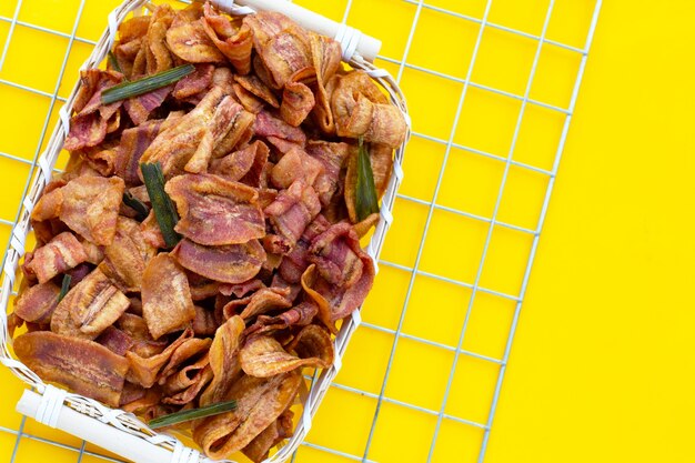 Banana slice chips in bamboo basket on yellow background.