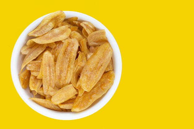 Banana slice chips in white plate on yellow background.