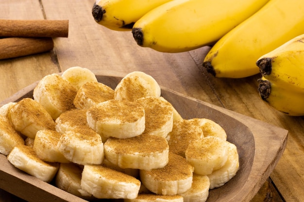 Banana slices with cinnamon sprinkled and cinnamon sticks with bunch of bananas in the background