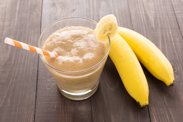 Banana smoothie and fresh banana on wooden background