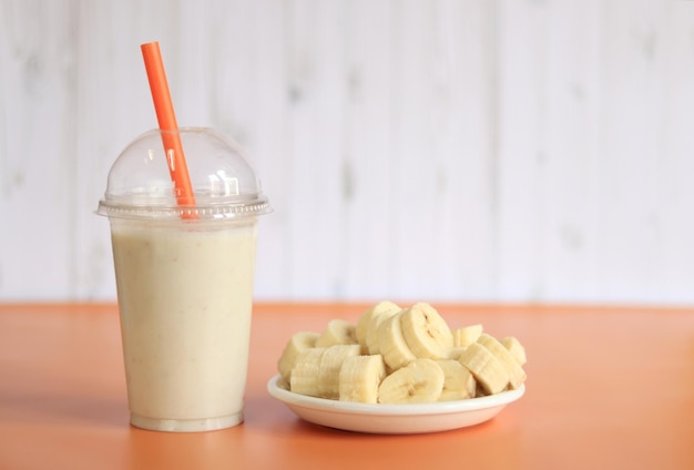 Banana smoothie with a plastic disposable cup a plate with a sliced banana next to it