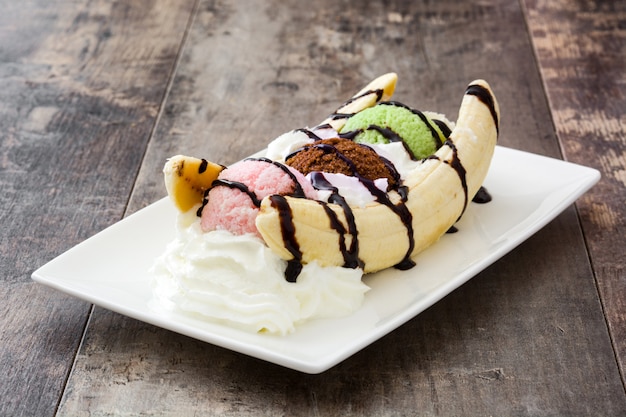 Banana split ice cream dessert with chocolate syrup on wooden