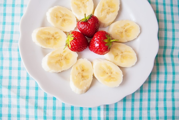 Banana and strawberries on a white plate and a colorful napkin.