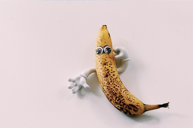 Banana with artificial eyes and hand on white background