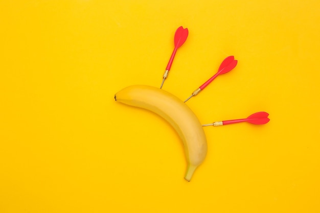 Фото Банан с дротиками на желтом фоне.