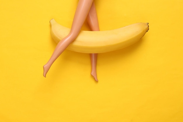 Banana with doll feet on yellow background Sex concept Minimalism Flat lay