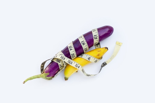 Banana with long purple eggplant wrapped in measuring tape on white background.