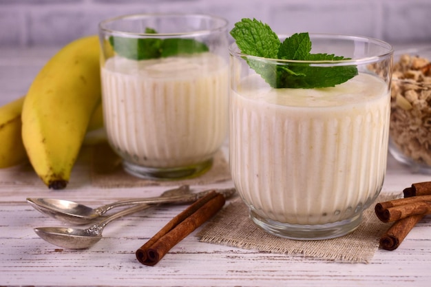 Banana yogurt with cinnamon and granola on a white wooden background.