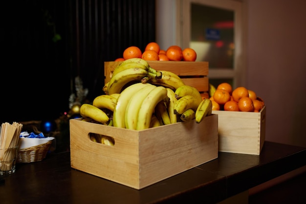 Bananen en mandarijnen in houten kisten op een donkere houten tafel tegen een donkere achtergrond.