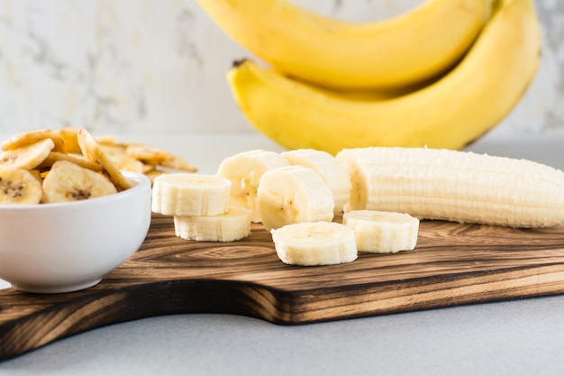 Bananenplakken op een snijplank en bananenchips in een kom op tafel. Fast food.