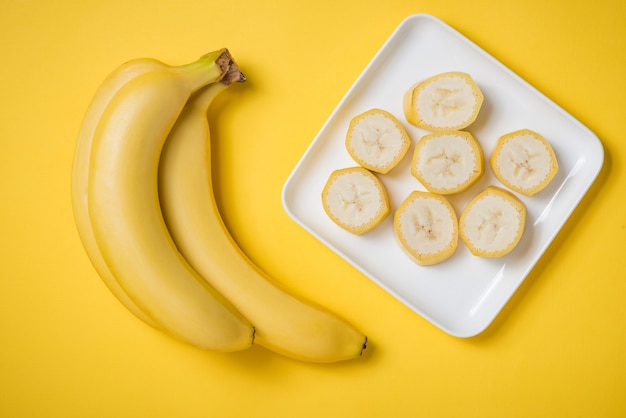 A banch of bananas and a sliced banana in a dish over yellow background.