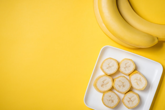 Банч бананов и нарезанный банан в блюде на желтом фоне.