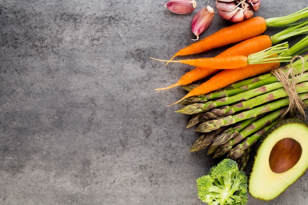 Banches of fresh green asparagus,  and vegetables on concrete surface, top view