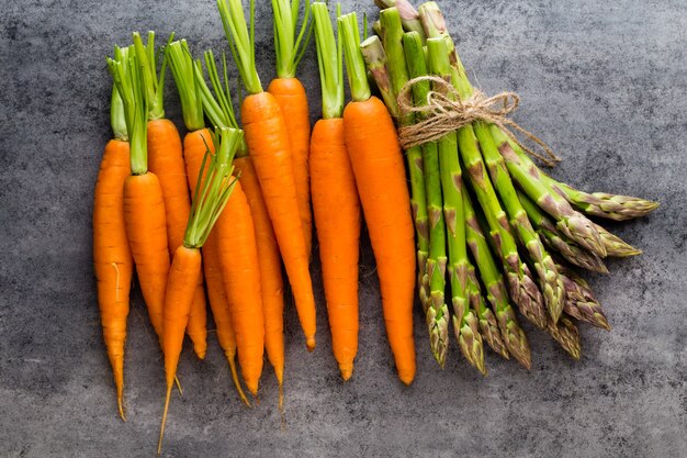 Banches of fresh green asparagus and vegetables on wooden table, top view