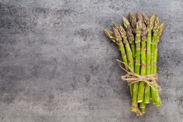 Banches van verse groene asperges en groenten op betonnen ondergrond, bovenaanzicht