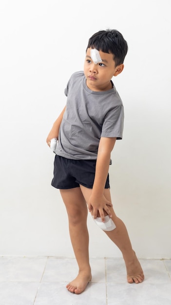 Bandage on forehead knee and finger Asian kid boy was accident injured while playing standing isolated on white background Life insurance
